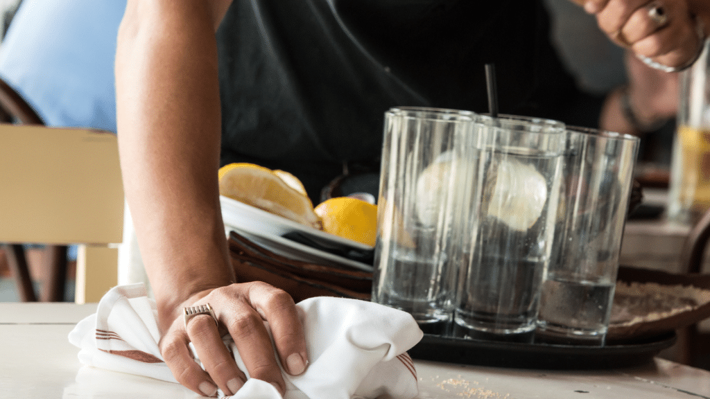 Server cleaning table with white cloth, holding tray of dishes