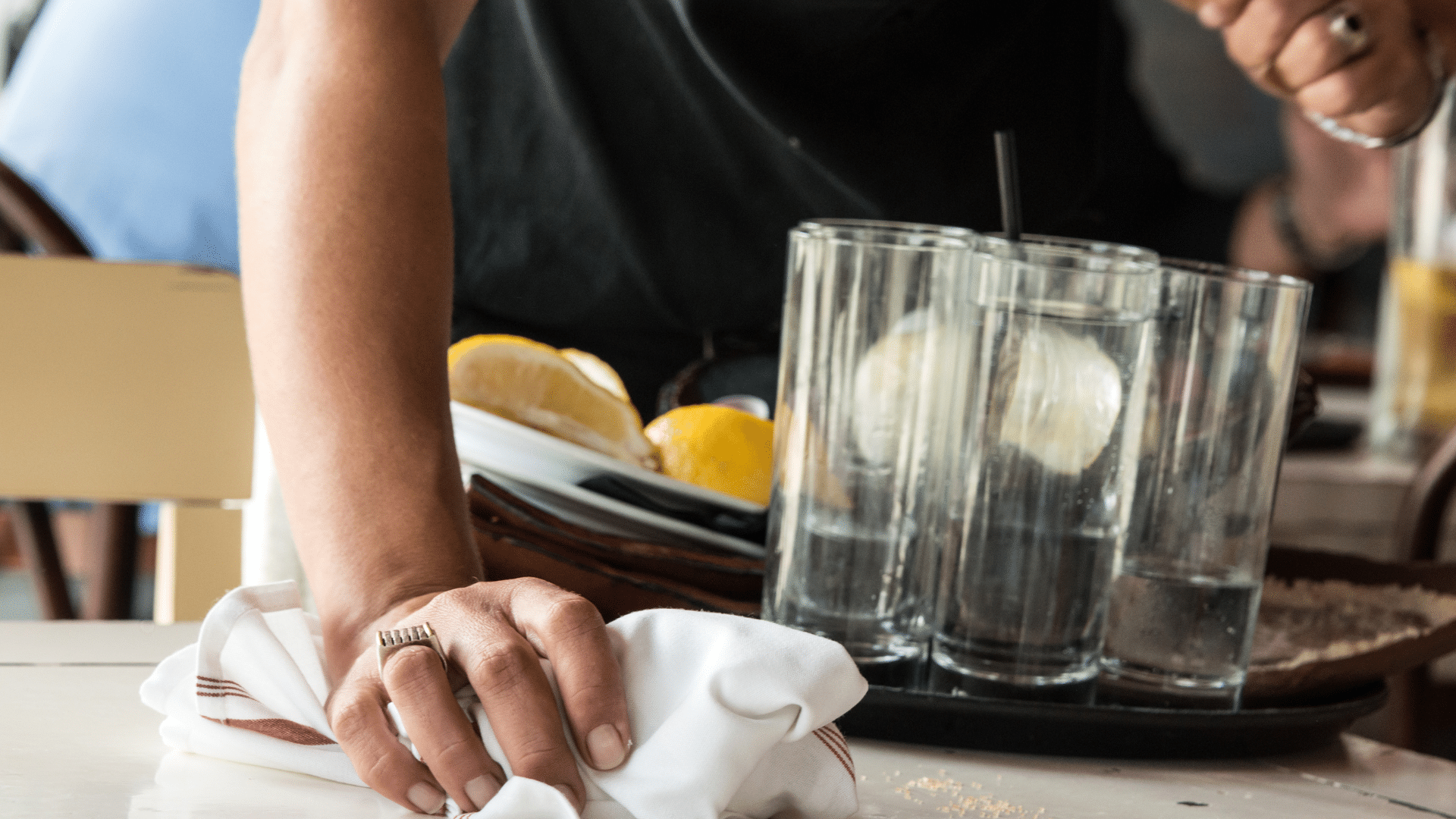 Server cleaning table with white cloth, holding tray of dishes