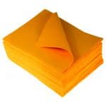Overhead perspective of a stack of TIDDOX orange liquid absorbent pads with the uppermost cloth gracefully curved to the left against a plain background.