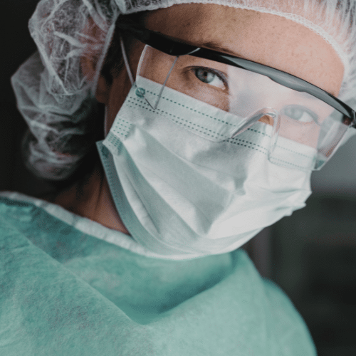 A woman donning a surgical mask and glasses, also wearing a hair cover for added safety.