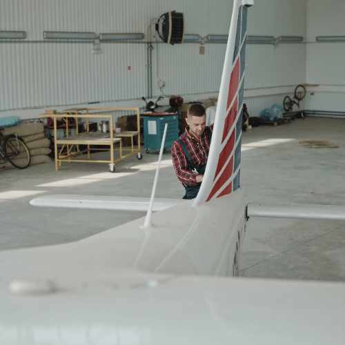 A man standing in a hangar, amidst airplanes and various tools.