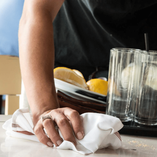 Server cleaning table with white cloth, holding tray of dishes